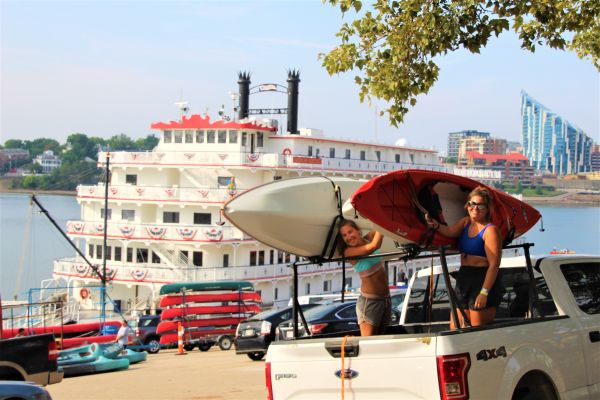 Outdoors_Ohio River Paddlefest 2023_Women in Truck with Kayaks_BB Riverboat and Ascent in Background (1)